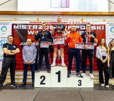 Hala sportowa. na podium osoby. Obok nich po obu stronach po dwie osoby