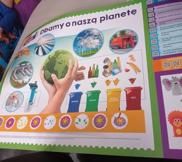 Pomieszczenie. Na stole leży duży plakat o głównym tytule "Dbamy o naszą planetę"