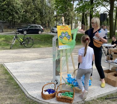 Na dworze. Skwer. Kobieta w towarzystwie dziewczynki odsłania tablicę informacyjną.