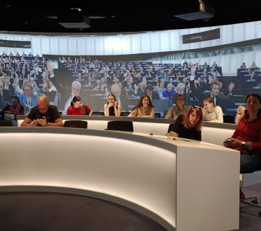 Pomieszczenie. Dwa półokrągłe, długie stoły przy których siedzą osoby