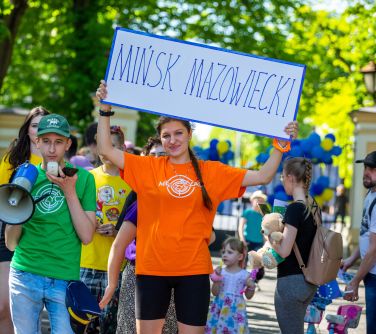 Dwór. Chłopiec w zielonej koszulce mówi przez megafon. Obok nastolatka w pomarańczowej koszulce trzyma w górze baner z...
