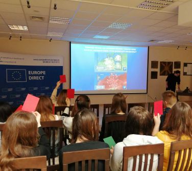 Aula. Na krzesłach siedza osoby. Słuchają wykąłdu. Na ekranie wyświetlana treść