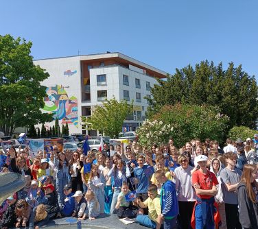 Na dworze. Grupa osób z flagami Europy pozuje przy fontannie. W tle drzewa i budynek