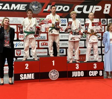 Hala. Na podium czterech chłopców w białych kimonach, dwóch na miejscu trzecim. Nagrody w dłoniach. Po obu stronach...