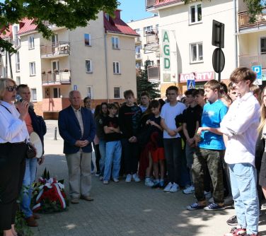 Na dworze. Zgromadzone nastolatki. Przed nimi tzy osoby dorosł. Kobieta w białej koszuli i czarnych spodniach przemawia do...