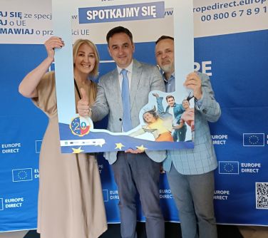 Trzy osoby roią sobie zdjęcie w jasno-niebieskiej ramce. W tle biało-niebieska ścianka