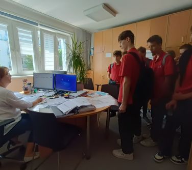 Pokój. Grupa nastolatków słucha opowieści kobiety siedzącej za biurkiem
