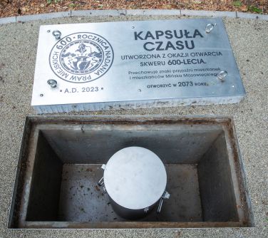 Dwór. Dół metalowy w chodniku, a w nim schowany metalowy pojemnik. Na pokrywie napis kapsuła czasu