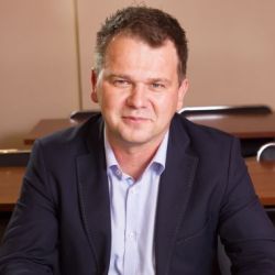 Zdjęcie portretowe. Mężczyzna uśmiecha się. Ma na sobie niebieską koszulę i granatową marynarkę.