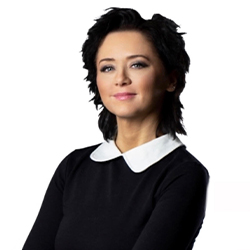 Zdjęcie portretowe. Kobieta z czarnymi włosami uśmiecha się. Ma na sobie czarną sukienkę z białym kołnierzykiem.