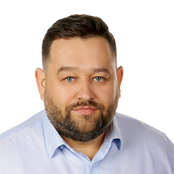 Zdjęcie portretowe. Mężczyzna uśmiecha się. Ma na sobie niebieską koszulę.