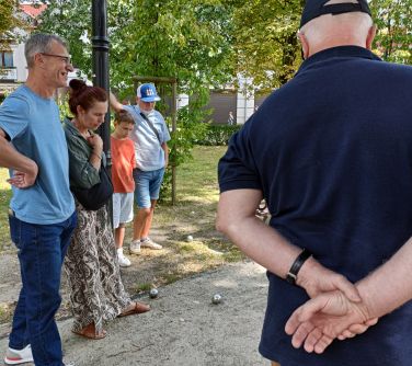 Alejka w parku, dzień. Na piaszczystej alejce leżą cztery metalowe kule. Naokoło osoby przyglądaja się.