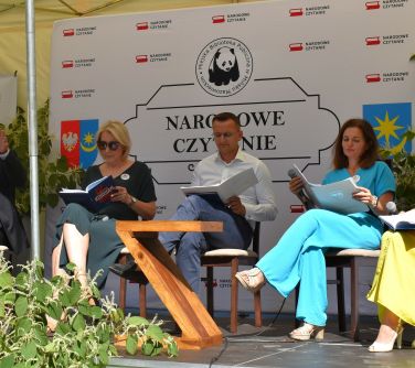 Dwór. Pięć osób siedzi na krzesłach pod jasnym namiotem czytają książkę