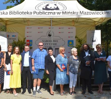Na dworze. Grupa osób pozuje stojąc przed jasnym namiotem