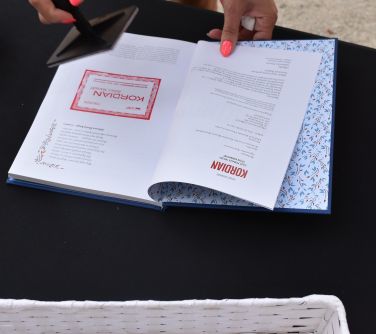 Na czarnej płachcie leży otwarta książka z czerwona pieczątką