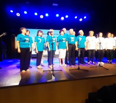 Na scenie wystepuje grupa seniorów w niebieskich i białych koszulkach