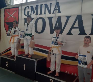 Hala sportowa. Na podium na poszczególnych miejscach, w białych kimonach zawodnicy. Na miejscu 3 dwie osoby