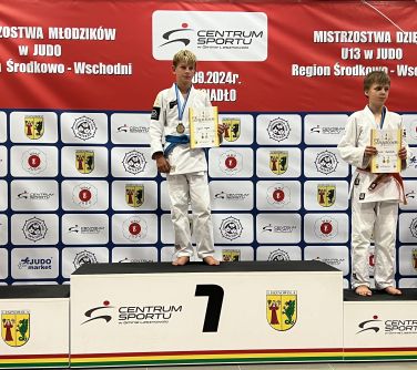 Hala sportowa. Na podium na poszczególnych miejscach, w białych kimonach zawodnicy. Na miejscu 3 dwie osoby