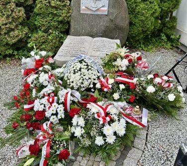 Pomnik z kamienia, przed nim kamienna księga. Na przodzie wiązanki z biało-czerwonych kwiatów i szarf. Naokoło małe...