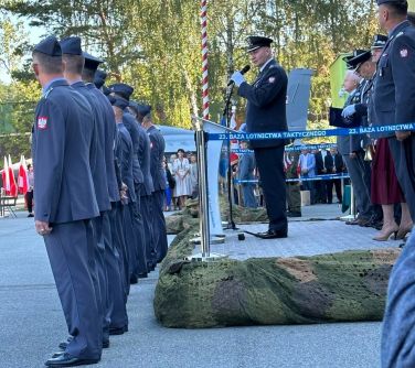 Na dworze, dzień. Na podwyższeni przemawia dowódca. Za nim i przed przed podwyższenie żołnierze w mundurach