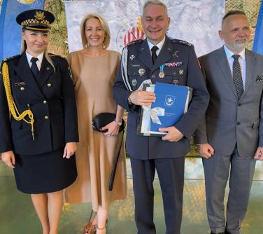 Pomieszczenie. Dwie kobiety jedna w mundurze strażnika i dwóch mężczyzn jeden w mundurze dowódcy pozują. Uśmiechają się.