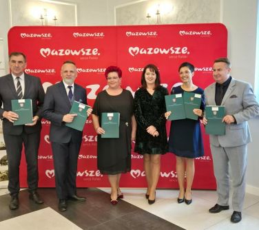 Pomieszczenie. Osoby pozują na tle dużego, czerwonego baneru