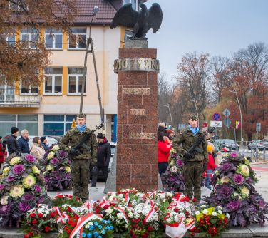 Na dworze, dzień. Przed pomnikiem wiązanki kwaitów. Po obu stronach żołnierze