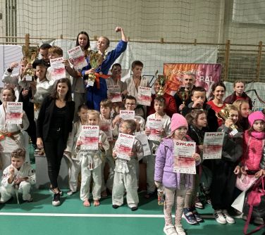Hala sportowa. Grupa osób i zawodników w białych kimonach. Dyplomy w dłoniach