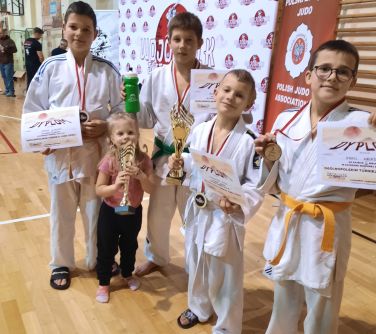 Hala sportowa. Pięcioro dzieci z dyplomami i pucharami. Czworo w białych kimonach