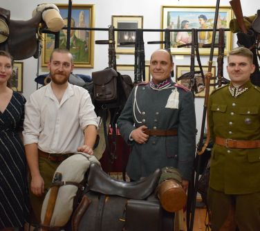 Wnętrze muzeum. Cztery osoby między siodłami. W tle na białej ścianie obrazy