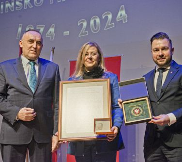 Pomieszczzenie. Trzy osoby pozują do zdjęcia. Kobieta trzyma obraz
