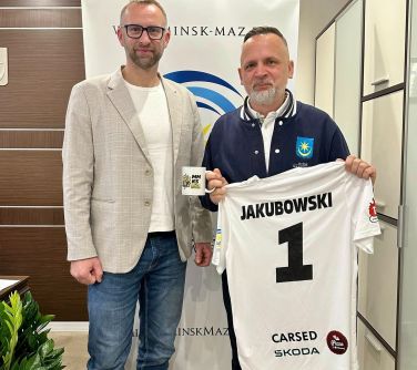 jasne pomieszczenie. Dwóch mężczyzn. Po prawj trzyma koszulkę