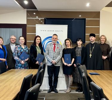 Pomieszczenie. Grupa osób pozuje na tle jasnego baneru