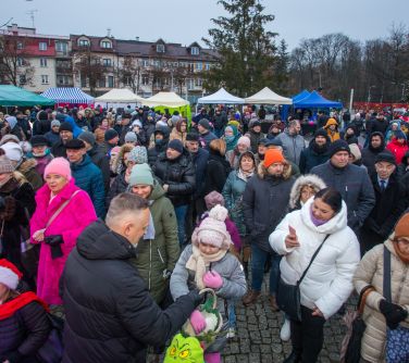 Na dworze, lekki zmierzch. Mężczyzna w czarnej kurtce dzieli się opłatkeim ze zgromadzonymi osobami