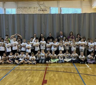 Oświetlona hala sportowa, dzień. Duża grupa dzieci i sześcioro dorosłych pozuje do zdjęcia