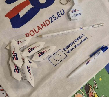 Jasna płócienna torba z logo niebiesko-czerwonym. Na niej kilka białych krówek z logo, dłupopis biały i ołówek