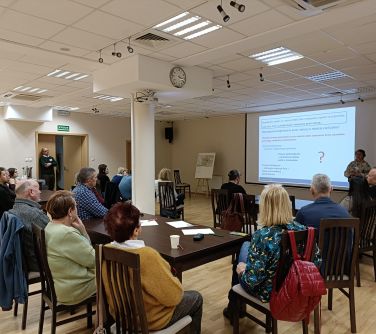 Oświetlona sala konferencyjna. Przy stolikach osoby słuchają wykładu