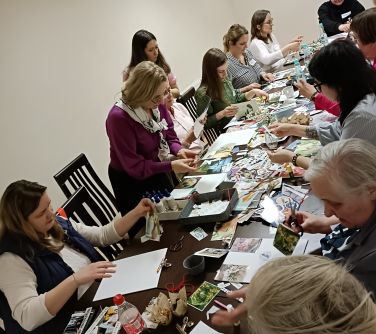 Sala konferencyjna. Przy długich stołach naokoło siedzą kobiety. Wykonuja pracę kolaże
