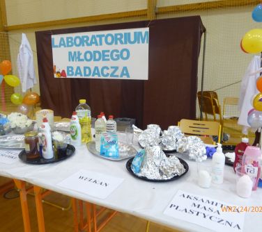Jasna sala gimnastyczna. Na długim stole soda, mąka, mydło, folia aluminiowa i inne rzeczy potrzebne do eksperymentów. W...
