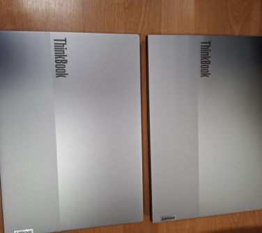 Na jasno-brązowym stole leżą dwa złożone szare laptopy
