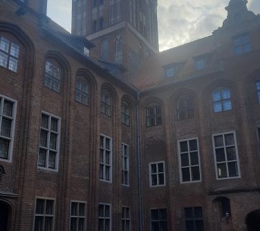 Na dworze, dzień. przed starym budynkiem z wieżą grupa osób