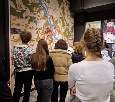 Oświetlone pomieszczenie. Na ścianie duża mapa. Osoby oglądają