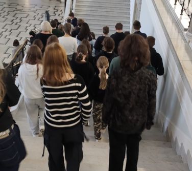 Oświetlony jasny budynek. osoby schodzą po białych schodach. Na przeciko białe chody do góry