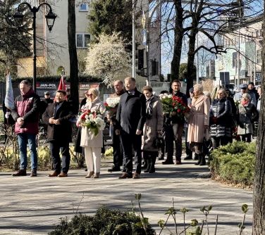 Na dworze, dzień, słońce. Grupa osób z wiązankami biało-czerwonymi