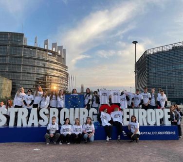 Na dworze, dzień. Grupa osób w białych koszulkach pozuje przy dużym białym napisie Strasbourg Europe