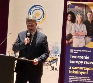 Mężczyzna do mikrofonu przemawia. W tle banery