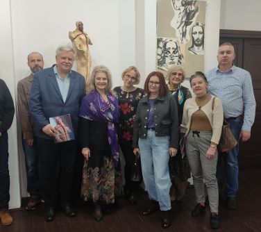 Oświetlone pomieszczenie. Grupa osób pozuje. W tle biała ścian az rzeźbą