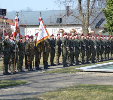 na dworze, słoneczny dzień. Grupa żołnierzy. Część z bornią, część z szablami. Dwie chorągwie