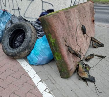 Dzień. Na chodniku oparte o beton stara opona, materac oraz worki