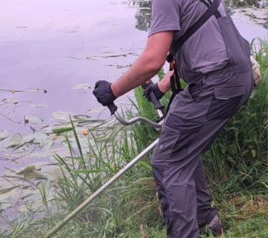 Na dworze, dzień. Mężczyzna nad brzegiem wycina trawe nad samą wodą